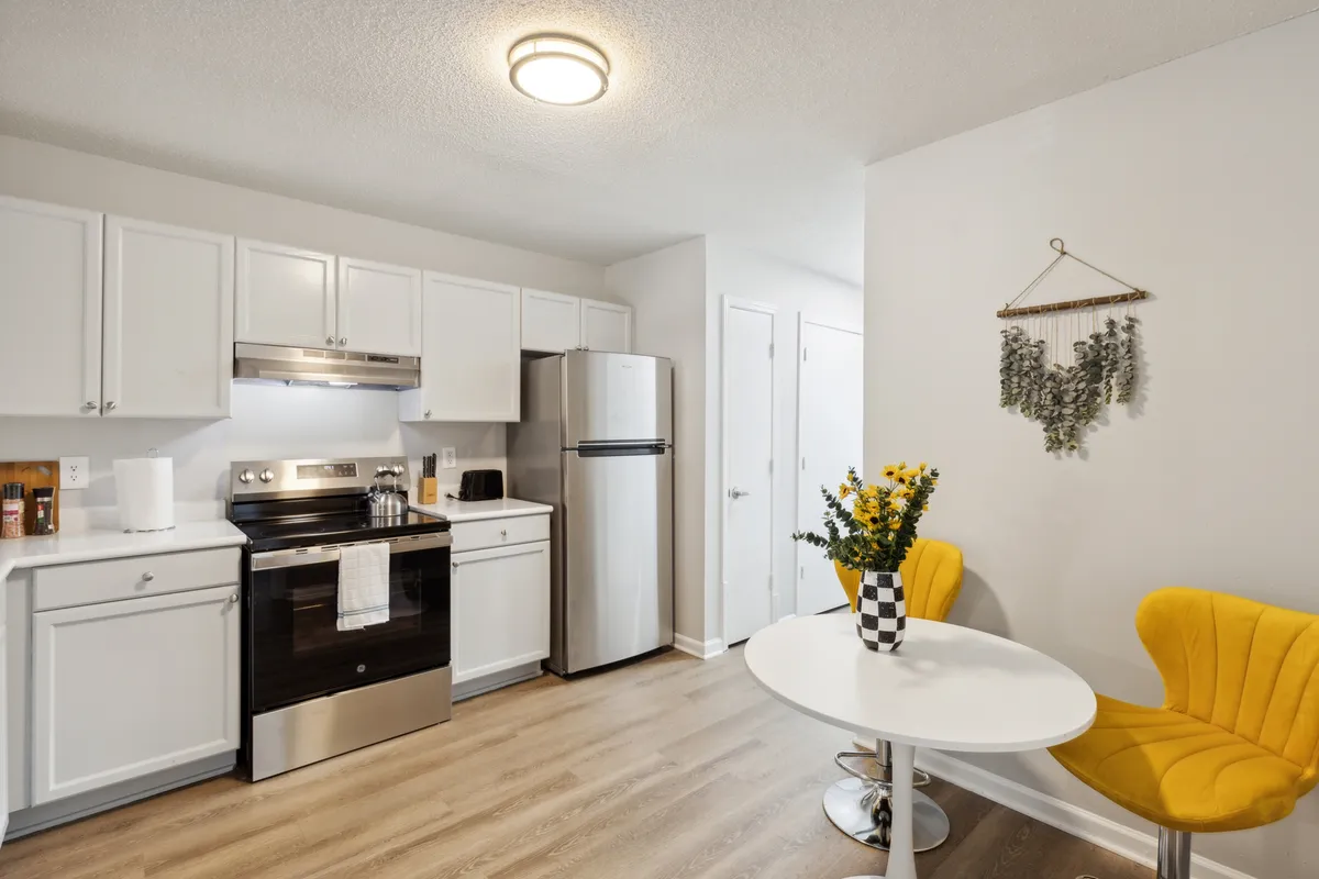 This bright, cheerful scene centers on a yellow chair and round dining table set against the backdrop of visible kitchen appliances. The area feels cozy and perfect for casual dining, morning coffee, or quick bites, with a playful pop of color that adds warmth to the experience.