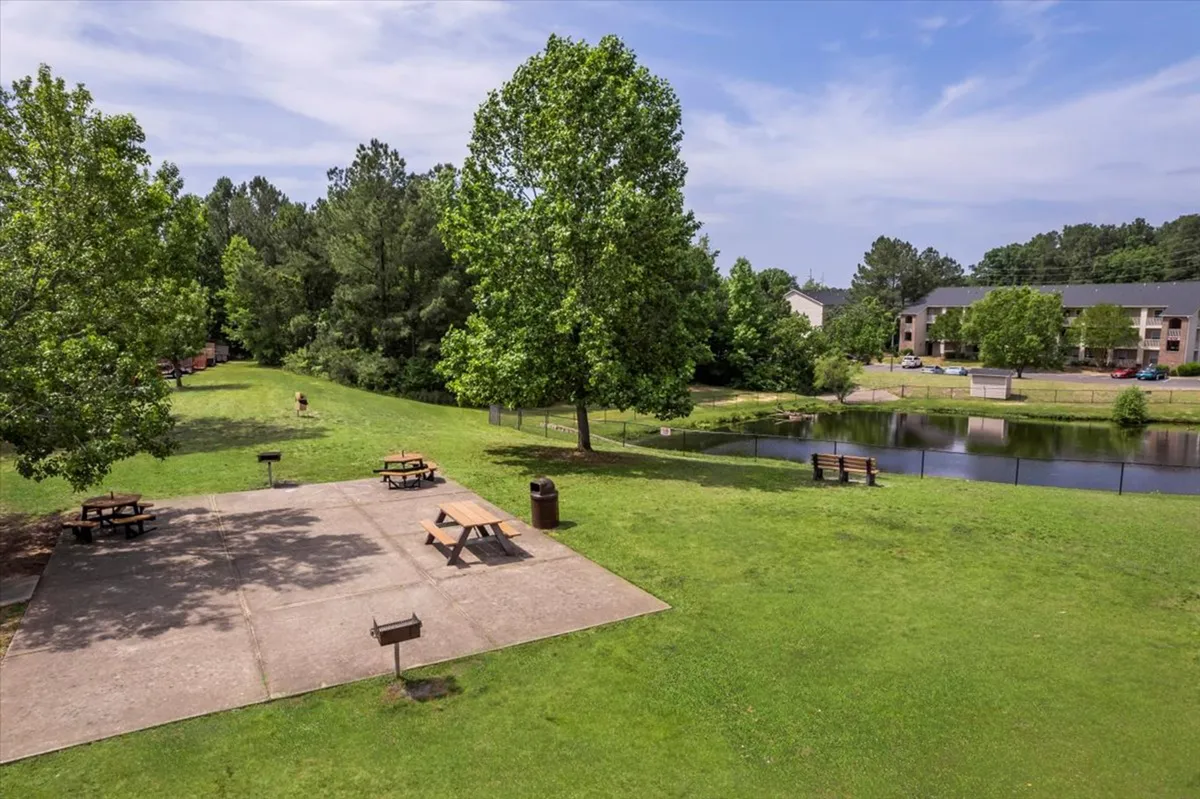 A tranquil exterior view showcases a picnic area by a pond, surrounded by trees and benches. The calming water, lush greenery, and open seating invite guests to relax outdoors or enjoy quiet, reflective moments.