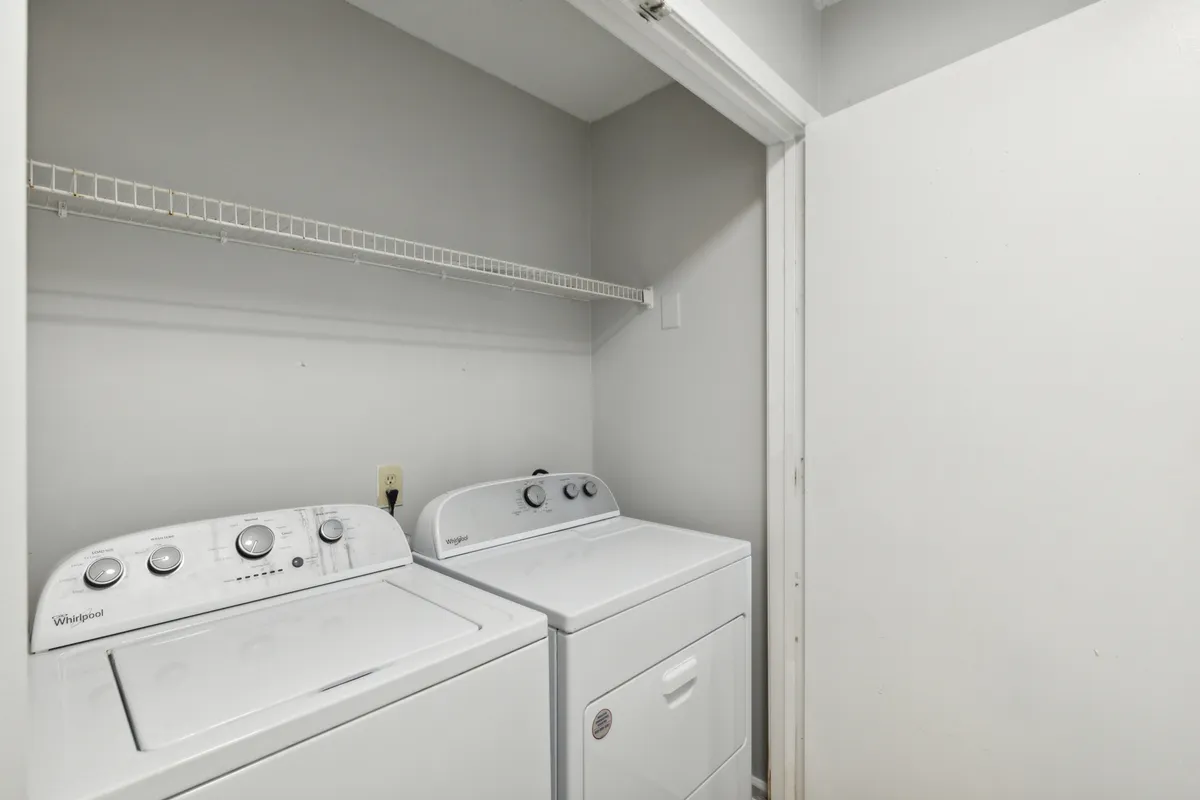 The image showcases a laundry area with a washing machine, dryer, and a neatly organized shelf above for laundry supplies. The space is clean and functional, evoking a sense of convenience for extended stays and family needs.