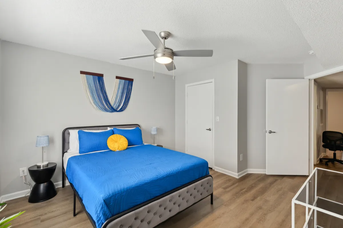 A cozy bedroom featuring a bed with blue bedding, a decorative wall hanging, and a nightstand with a lamp. The space feels calm and restful, perfect for unwinding after a busy day of activities.