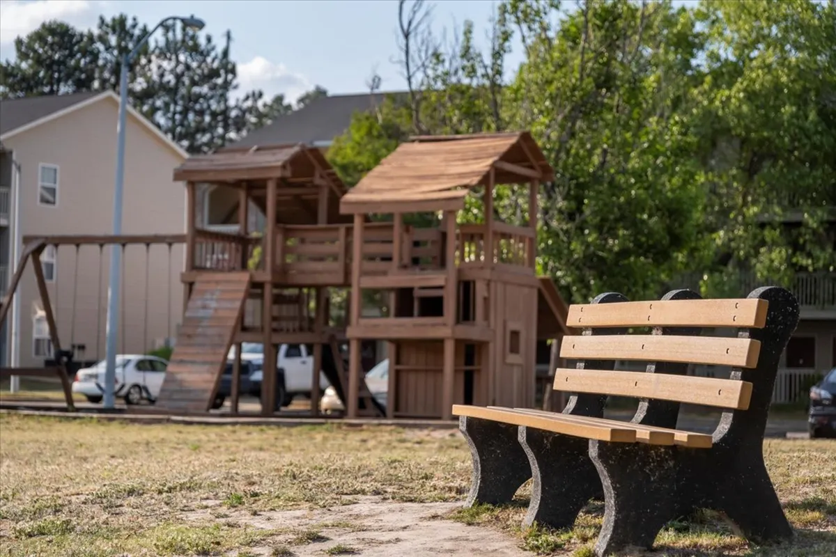 This image captures a cheerful playground structure and a nearby bench, set within a communal outdoor area. The scene is lively and suggests a space for children to play while families gather and relax together.