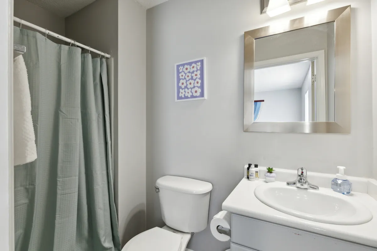 A bright, modern bathroom with a stylish mirror above the sink, soothing wall art, and a soft shower curtain. The design supports both privacy and relaxation, ideal for unwinding after a busy day or preparing for one.