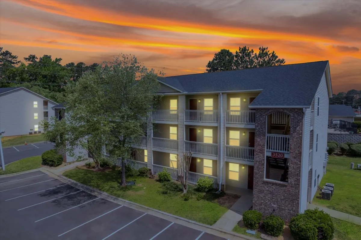 This image shows the apartment building's facade at dusk, highlighted by a sunset sky and warmly lit windows. Several balconies are visible, suggesting spaces for relaxation or informal gatherings, and the overall scene radiates a welcoming, after-work atmosphere.